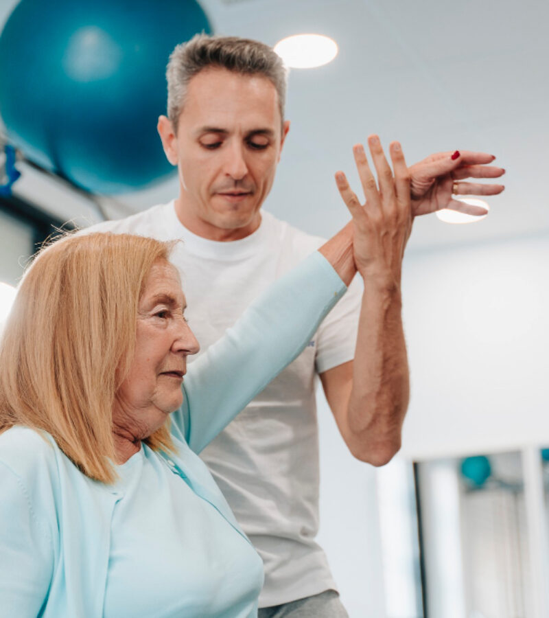 frau-in-ihren-70ern-die-von-einem-physiotherapeuten-in-ihren-40ern-unterstuetzt-wird-um-die-volle-beweglichkeit-der-arme-wiederzuerlangen